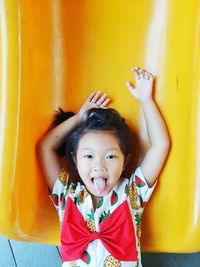 High angle portrait of cute girl with arms raised sticking out tongue on slide