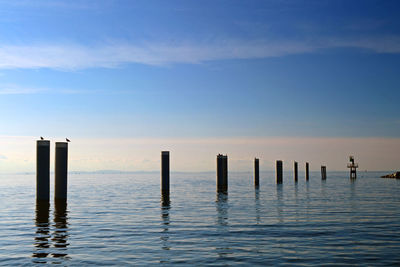 Wooden posts in sea against sky at sunset