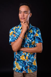 Young man looking away while standing against black background