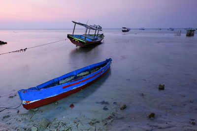 Boat moored on beach against sky during sunset