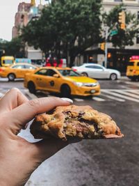 Cropped hand holding food on road in city