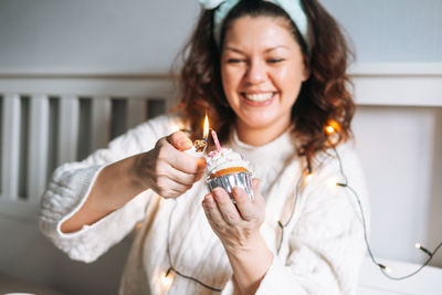 Young adult woman body positive in white sweater with festive cupcake with candle in hands 