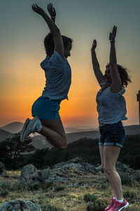 Full length of friends jumping against sky during sunset