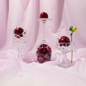 Still life arrangement of cristal glasses filled with red plums against light violet background. 