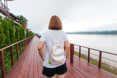 Rear view of woman standing on promenade by river