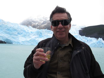 Portrait of young man holding sunglasses against mountain