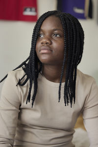 Contemplative female teenager with braided hair sitting at home