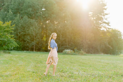 Young caucasian woman or girl in a summer dress and a denim shirt is walking on the grass