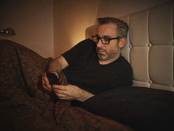 Relaxed and serious man in bed reading on the internet with a smartphone before sleeping and resting