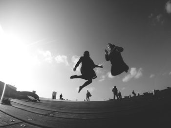 Low angle view of people jumping against sky