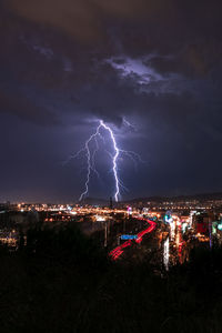Lightning over illuminated cityscape against sky at night