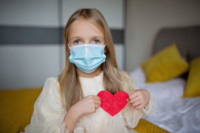 Portrait of girl wearing mask and holding heart shape at home