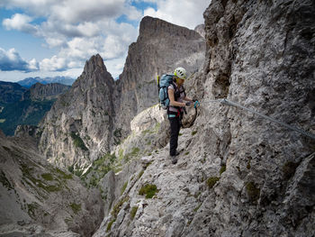 Full length of woman climbing on cliff against mountains