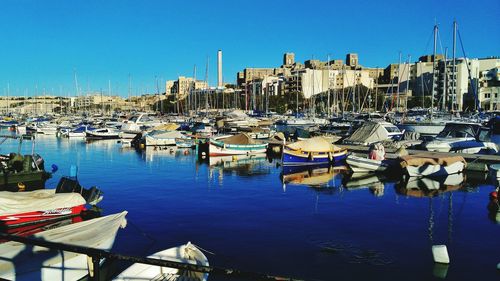 Boats moored at harbor against clear blue sky