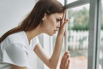 Young woman looking away through window at home