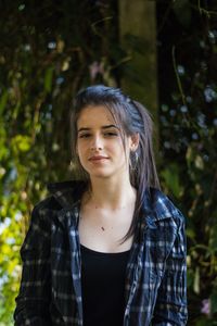 Portrait of beautiful young woman standing against trees