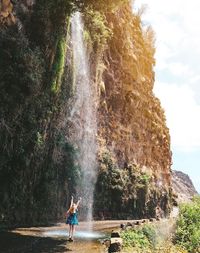 Woman standing by rock formation and waterfall