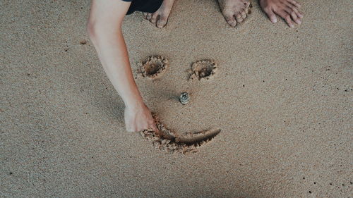 Low section of man making anthropomorphic smiley face in sand at beach