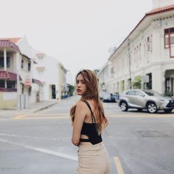 Portrait of young woman standing on road in city