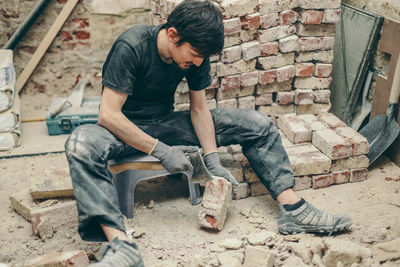 A young man cleans bricks with an axe.