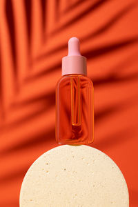 Cosmetic bottle with serum or oil on podium. orange background with daylight and palm shadow