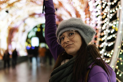 Smiling young woman on well decorated town square with christmas lights wearing glasses