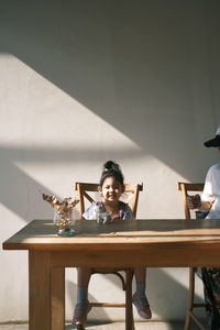 Portrait of girl sitting on table against wall