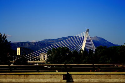 Suspension bridge in city against clear blue sky