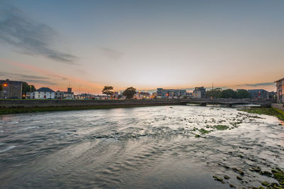 Scenic view of river by buildings against sky during sunset