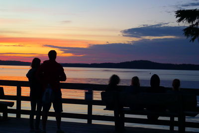 Silhouette people sitting on pier at sunset