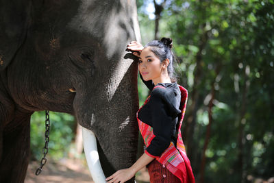 Young woman touching elephant while standing against trees