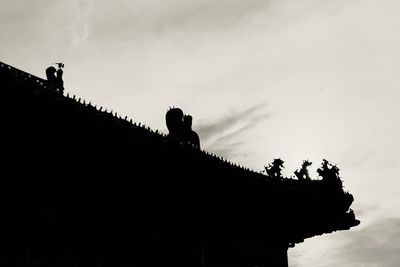 Low angle view of silhouette building on roof against sky