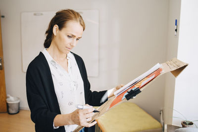 Confident businesswoman writing strategy on placard at creative office