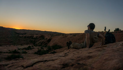 Rear view of man sitting on land against sky during sunset