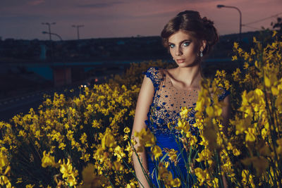 Portrait of beautiful young woman standing by yellow flowering plants