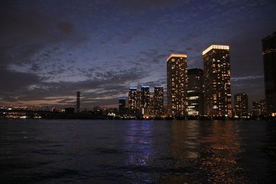 Illuminated city by sea against sky at night