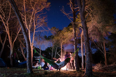 People on bare tree against sky at night