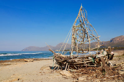 Driftwood ship on beach against clear blue sky