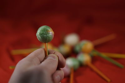 Cropped hand holding colorful lollipop over red fabric