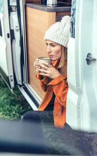 Woman drinking coffee sitting at the door of a campervan