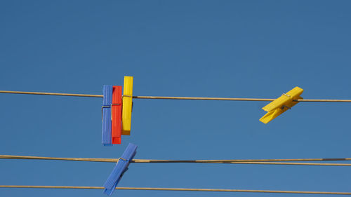 Low angle view of clothespins on clothesline against clear blue sky