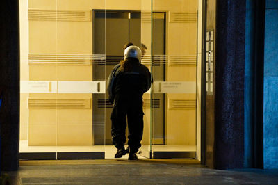 Rear view of woman wearing protective workwear while walking by glass door