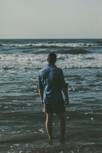 Rear view of man standing on beach against clear sky