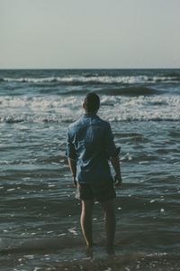 Rear view of man standing on shore at beach