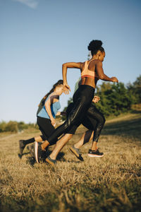 Male and female athletes running on grass against sky in park