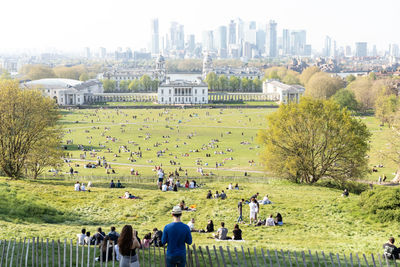 People on field by buildings in city against sky