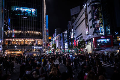 Crowded street by illuminated buildings in city at night