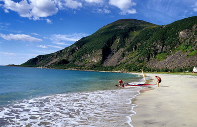 Mid distance view of friends by boat on shore at beach