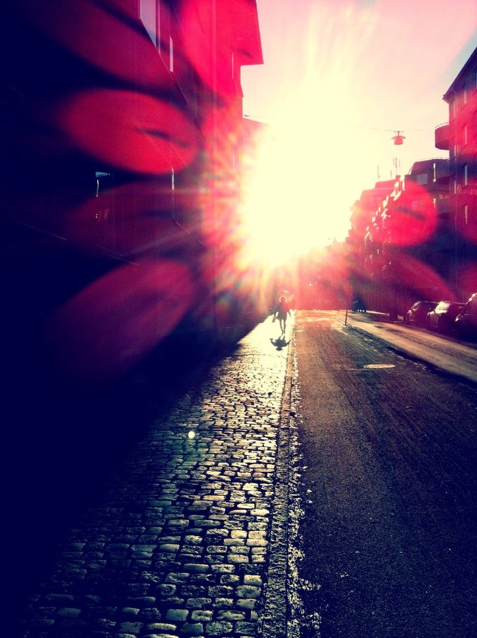 sun, transportation, street, sunlight, sunbeam, lens flare, the way forward, building exterior, sunset, built structure, architecture, road, car, city, cobblestone, land vehicle, surface level, red, mode of transport, sidewalk