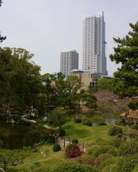 Park by buildings in city against sky